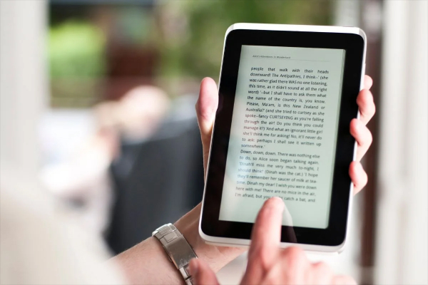 Person reading an e-book on a smartphone, with a Kindle and paper books nearby.