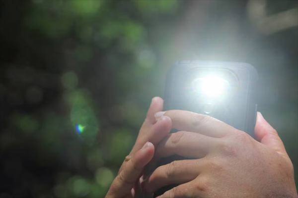 Smartphone flashlight illuminating a dark room, replacing a traditional handheld flashlight.